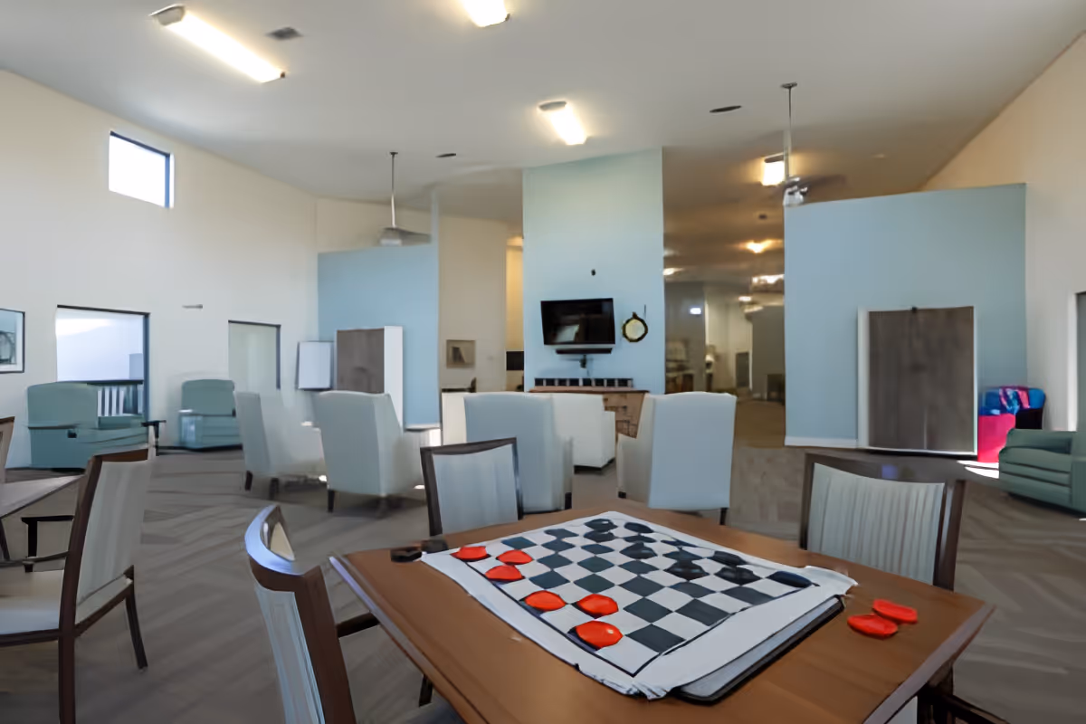 Spacious senior living common room with seating, a wall-mounted TV, and a table set up with a checkerboard game.
