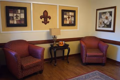 Two red patterned armchairs flank a side table with lamp in a lounge with wall art.