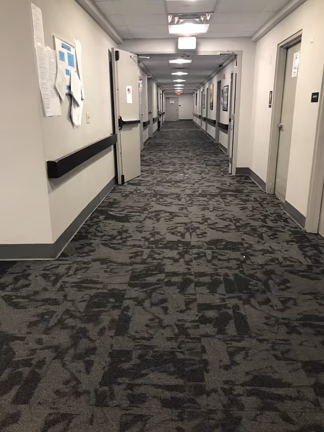 Long carpeted interior corridor with handrails, several doors, and overhead lights.