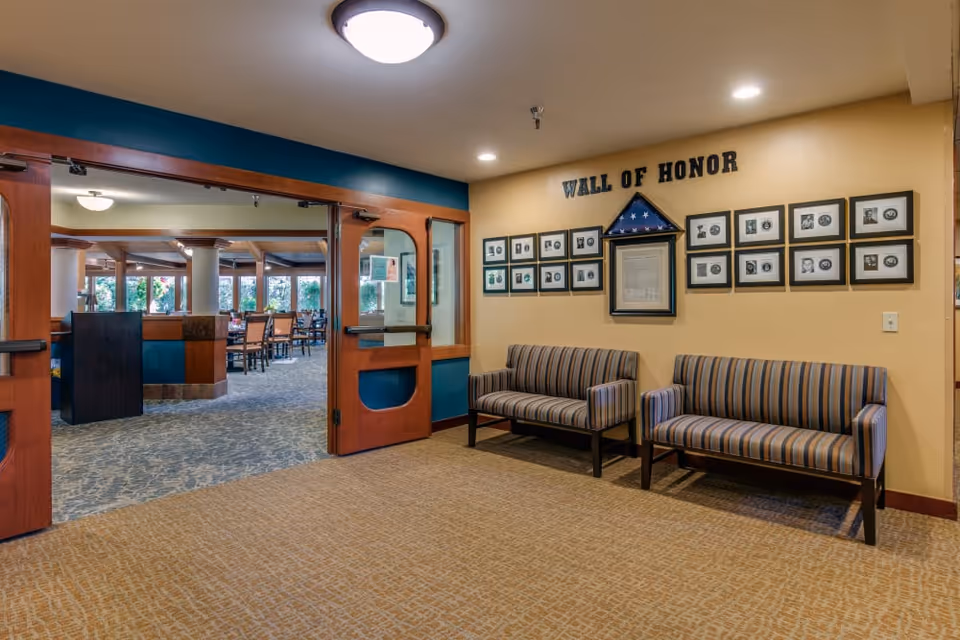 A seating area with two striped benches beneath a 'Wall of Honor' photo display and double doors opening to a dining room.