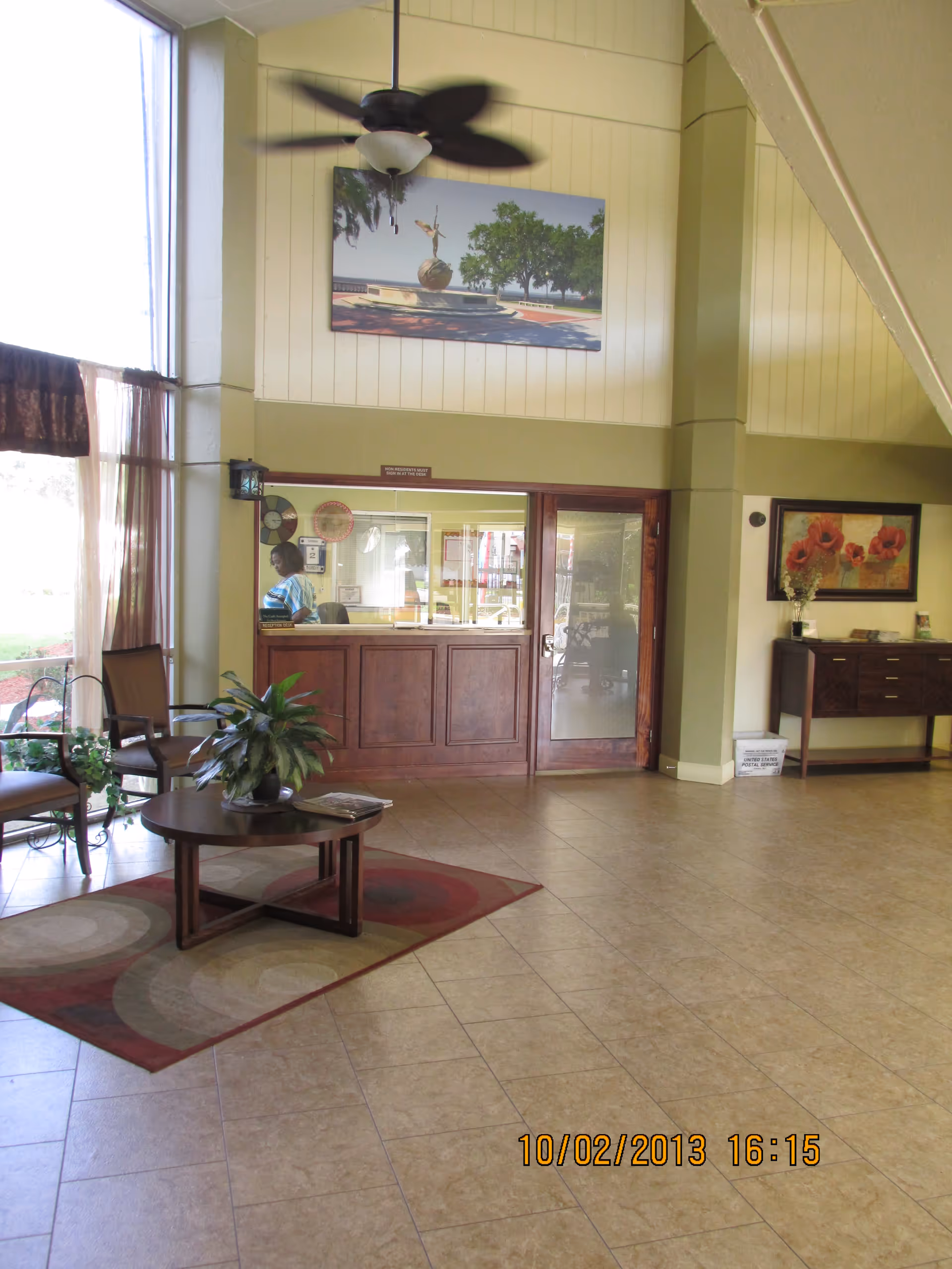 Lobby interior with a reception window, seating area and coffee table under a ceiling fan.