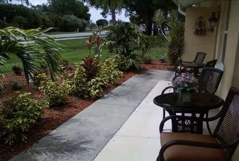 Outdoor patio with chairs and a glass table along a landscaped walkway beside a building.