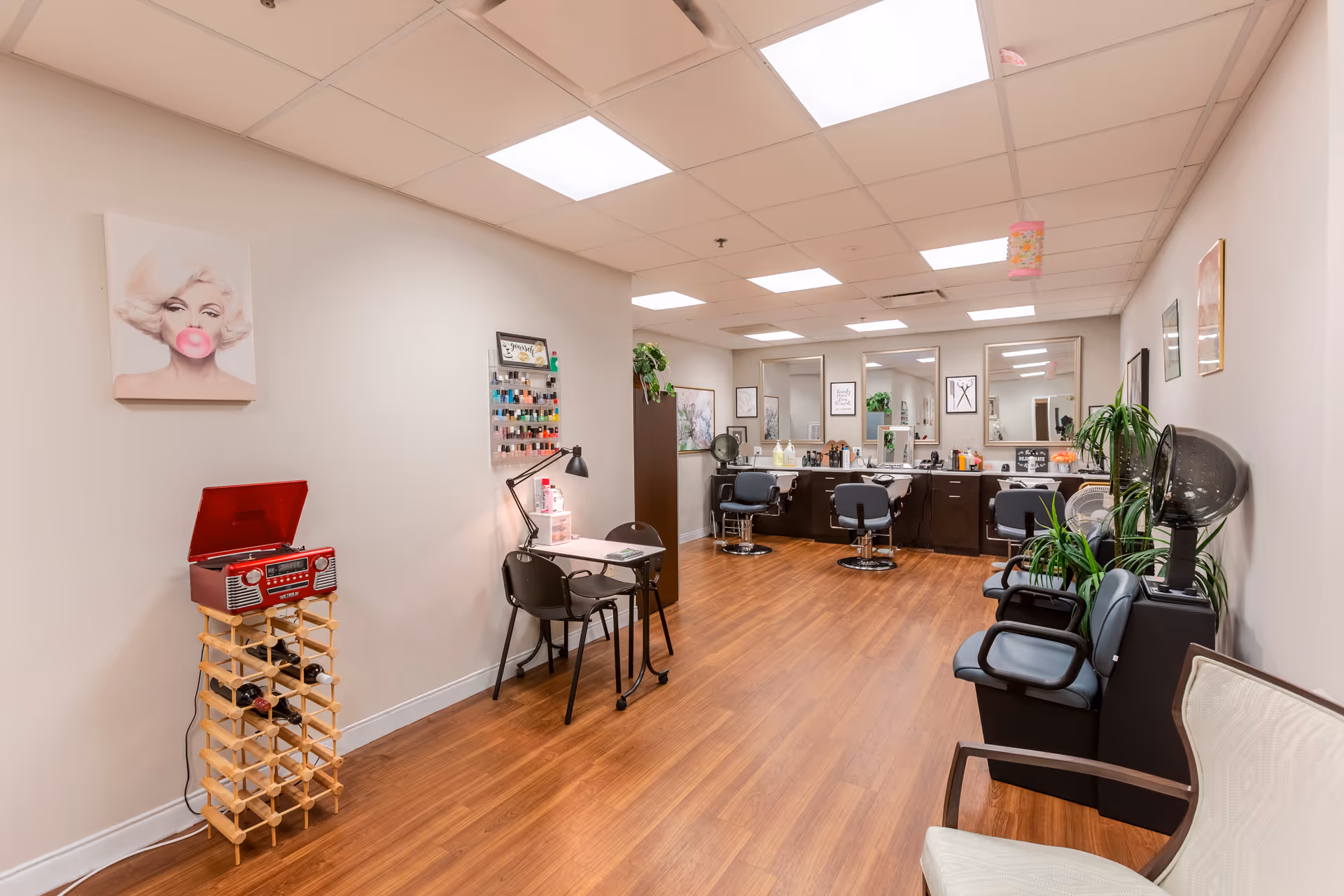 Bright salon interior with styling chairs and mirrors, a manicure table, hair dryers and wood flooring.