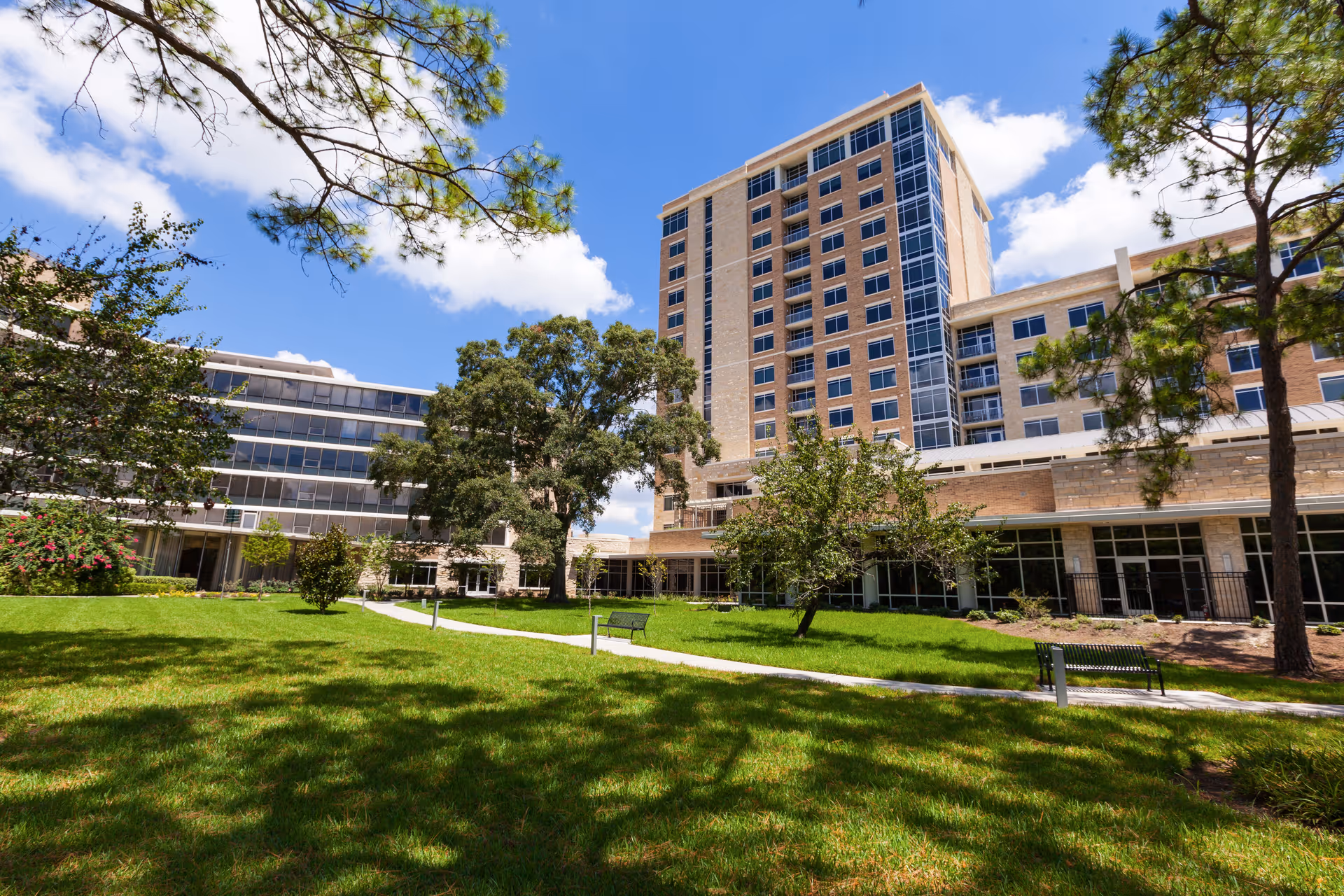 Exterior view of a multi-story senior living building with a green courtyard and benches.