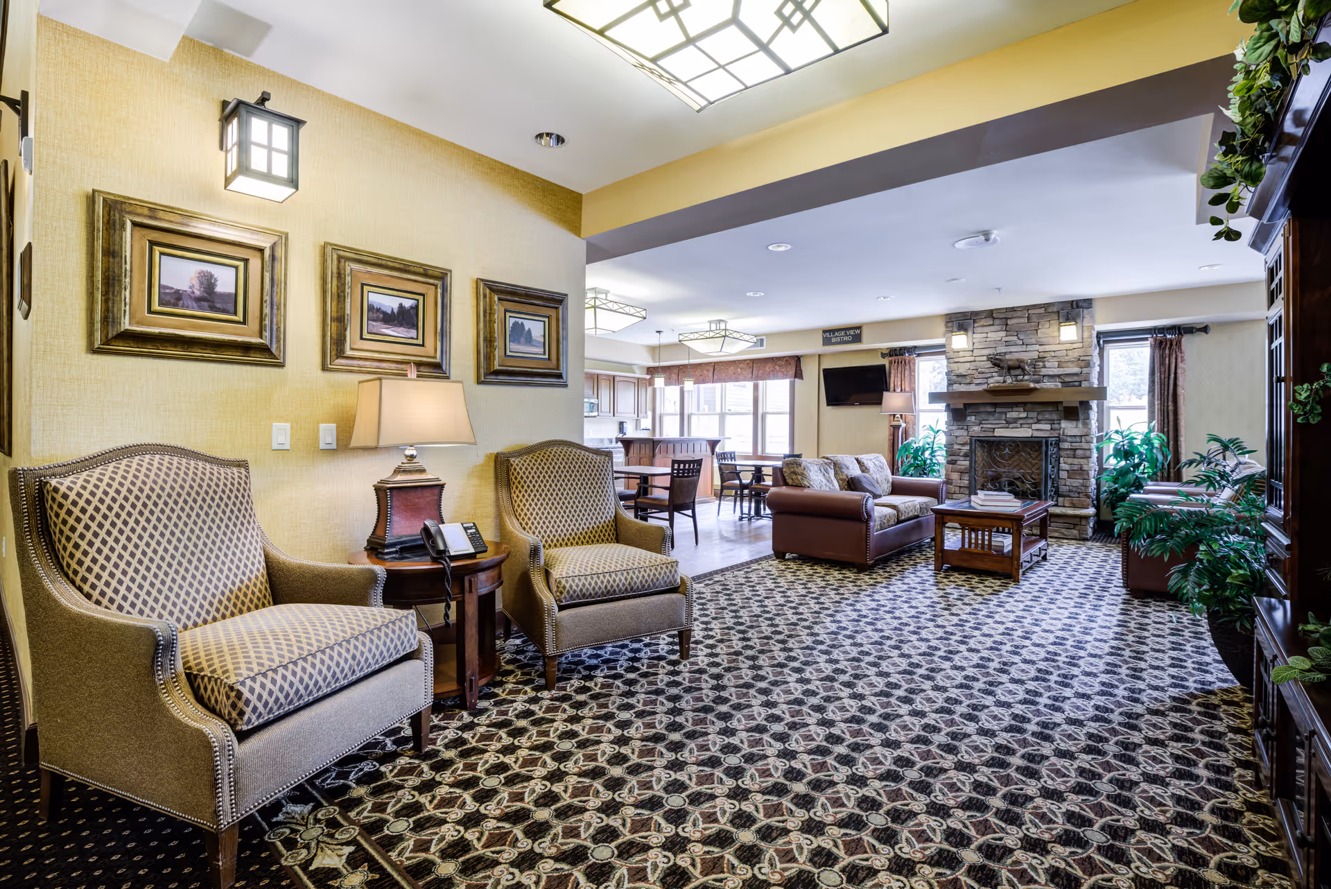 Spacious communal lounge with patterned armchairs, sofas, a stone fireplace and adjoining dining area.
