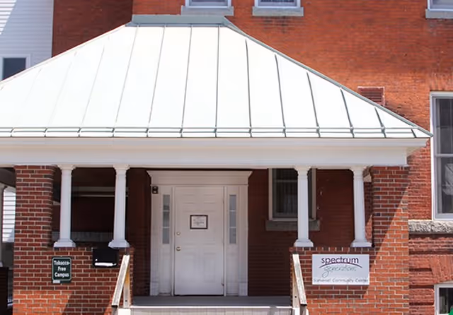 Entrance of a brick building with a white door under a white metal roof supported by white columns. There are signs on either side of the entrance, one reads 'Tobacco Free Campus' and the other reads 'spectrum generation Somerset Community Center'.