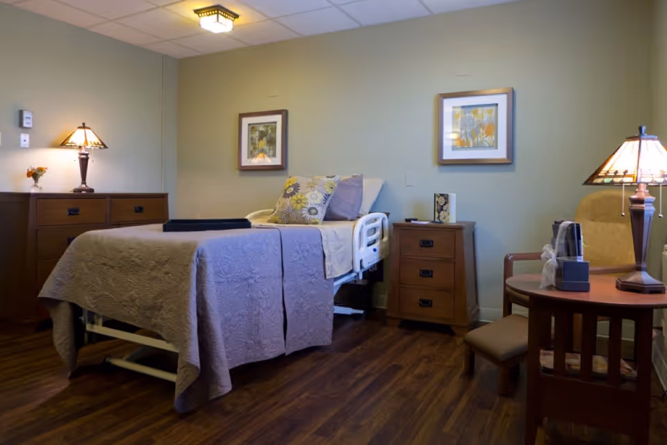 A furnished senior bedroom with an adjustable bed, wooden nightstands and lamps, a chair and small table on wood flooring.