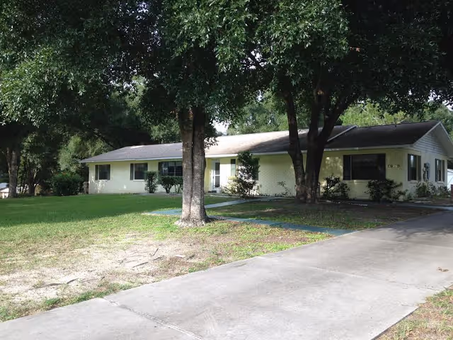 Exterior view of a single-story senior living building with a lawn and trees.