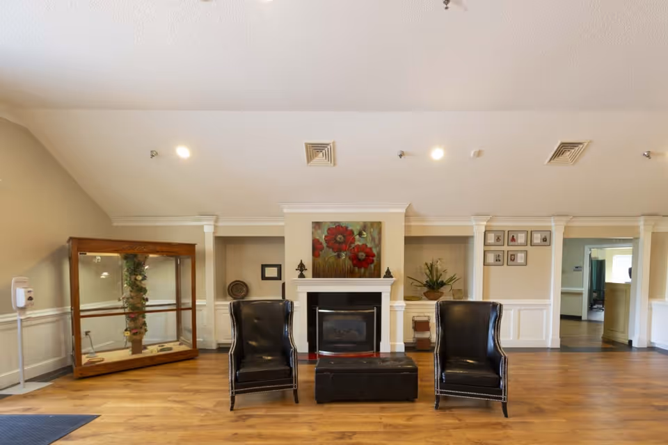 Lobby-style sitting area with two black leather chairs and an ottoman facing a fireplace topped by a floral painting.