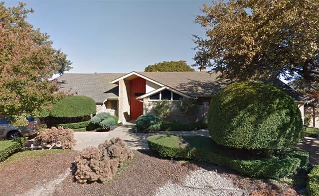 One-story brick building with a red front door, a driveway and neatly trimmed round shrubs in the front yard.