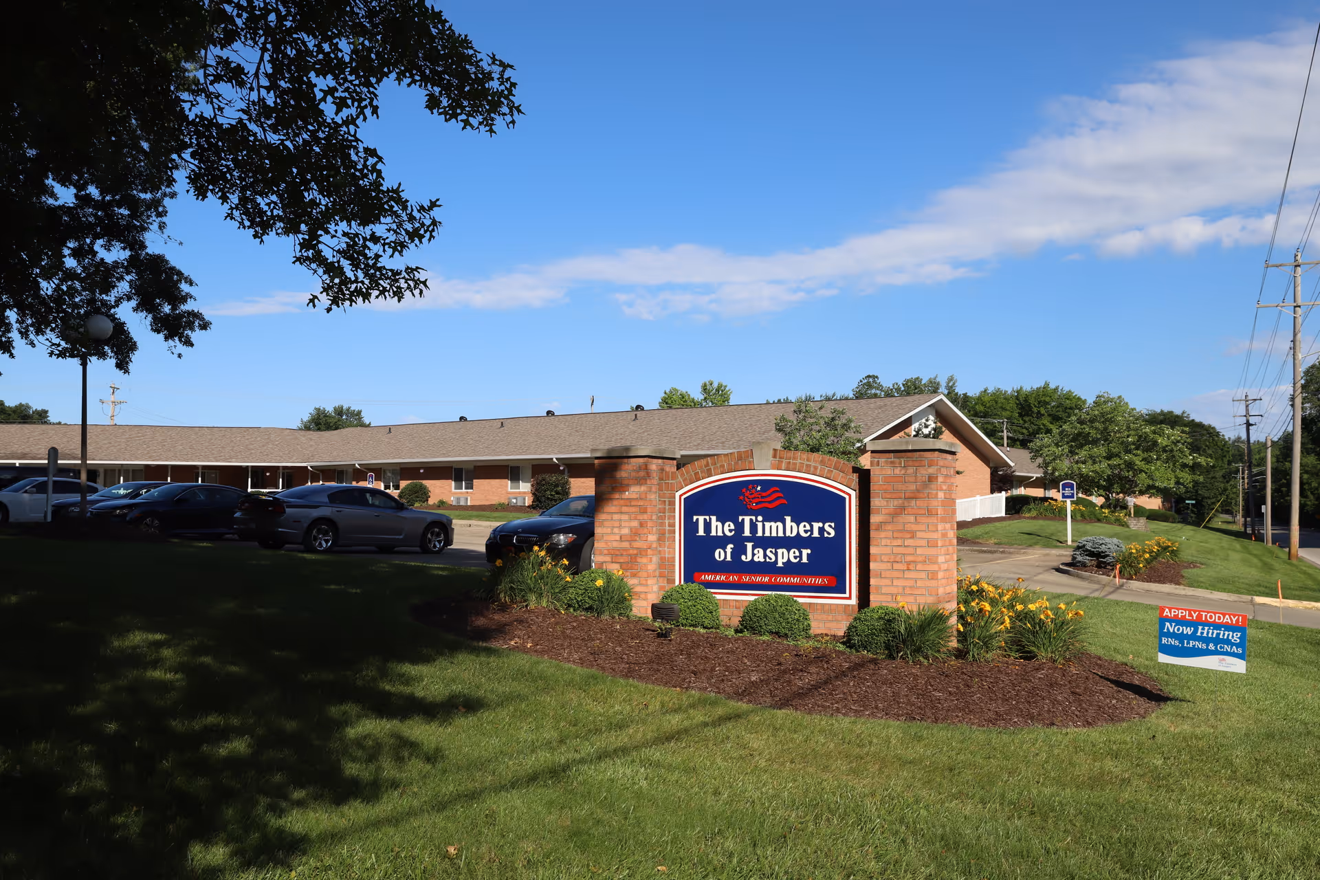 Brick entrance sign reading 'The Timbers of Jasper' on a landscaped lawn in front of a single-story senior living building.