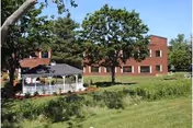Brick rehabilitation and healthcare building with a white gazebo, trees, and a grassy lawn under a blue sky.