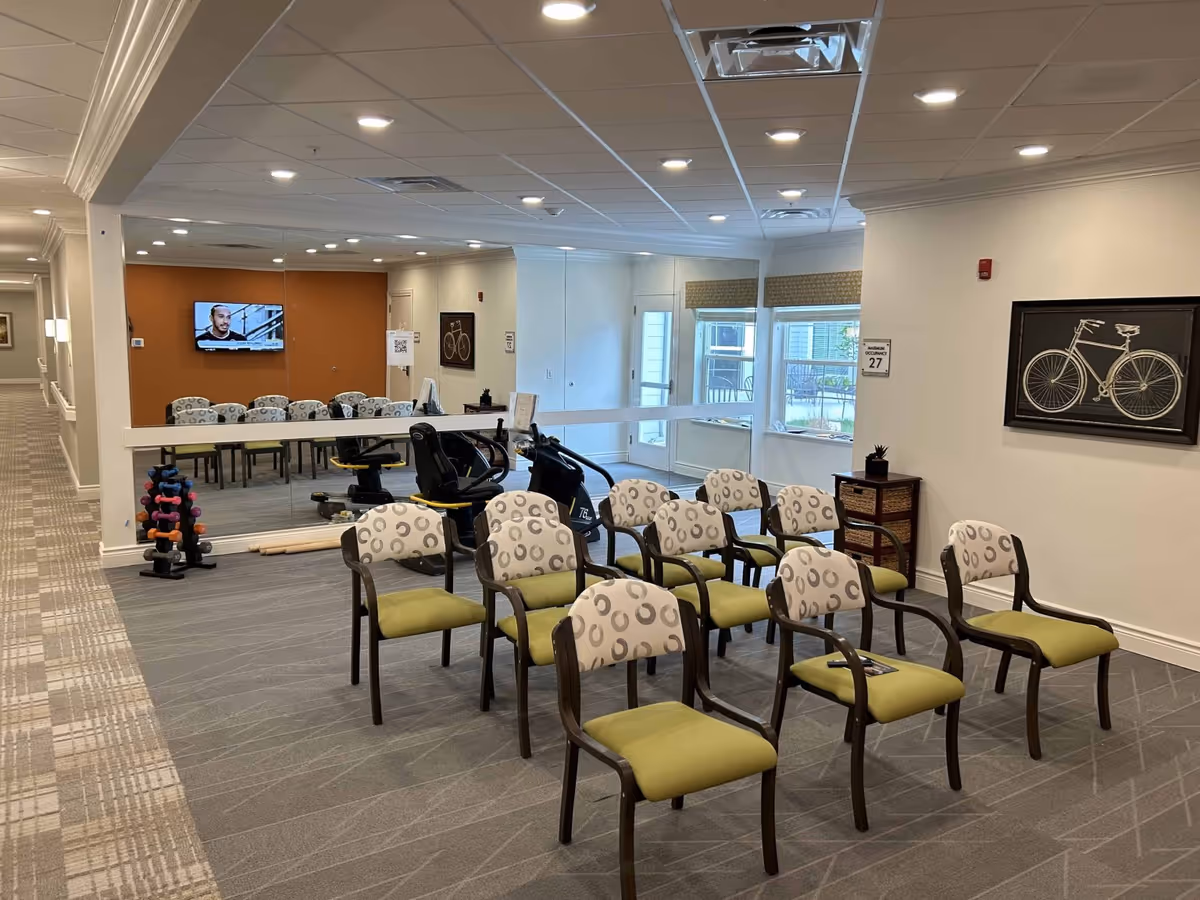 Well-lit interior common/activity room with rows of chairs, exercise equipment, a wall mirror and a television.