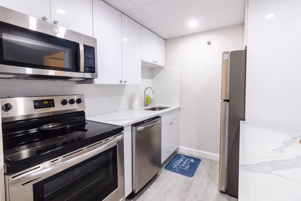 Small modern galley kitchen with stainless steel appliances, white cabinets, and a sink.