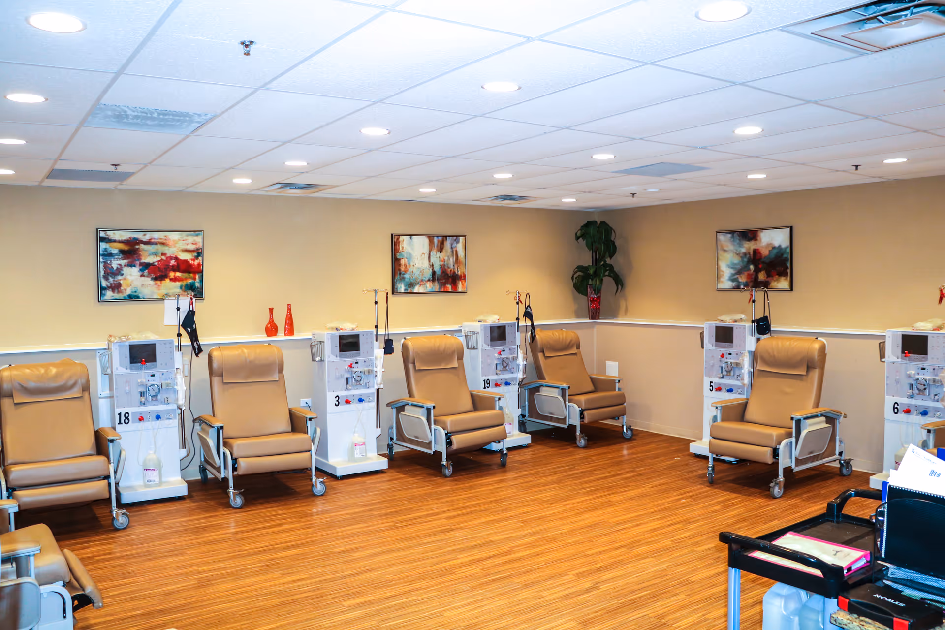 A clinical treatment room with multiple reclining chairs and dialysis machines arranged along the walls.