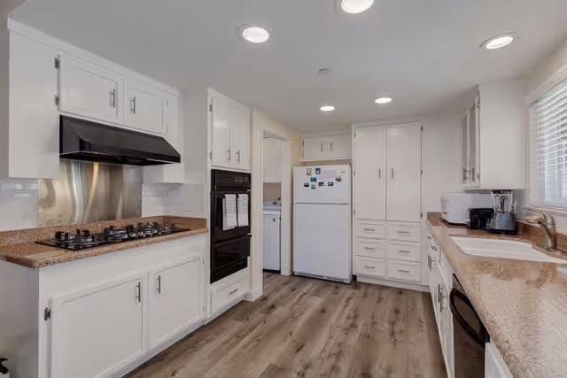 Bright modern kitchen with white cabinets, granite countertops, a gas cooktop and range hood, refrigerator, and wood-look flooring.