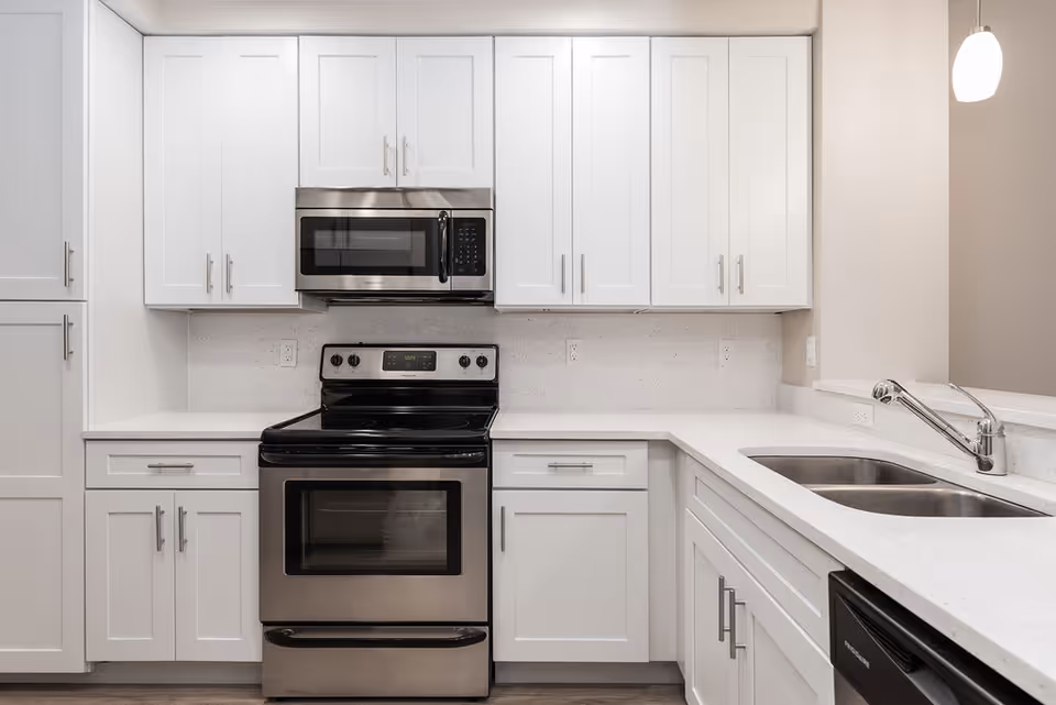Modern kitchen with white cabinetry, stainless steel electric stove and microwave, white countertops, double sink, and a hanging pendant light.