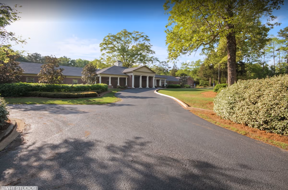 Front entrance of a single-story brick building with a porte-cochère, circular driveway and landscaped trees and bushes.