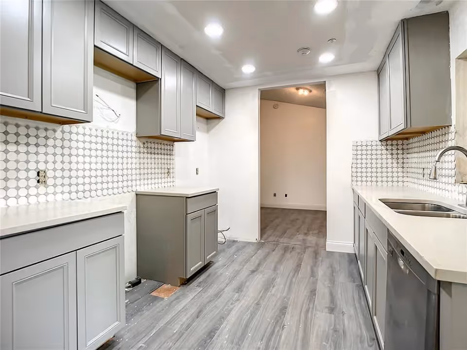 Modern galley-style kitchen with gray cabinets, white countertops, hexagonal tile backsplash and a stainless sink.