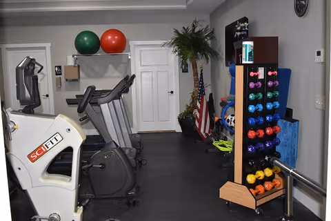 Small indoor fitness room with treadmills, a stationary bike, exercise balls, and a rack of colorful dumbbells.