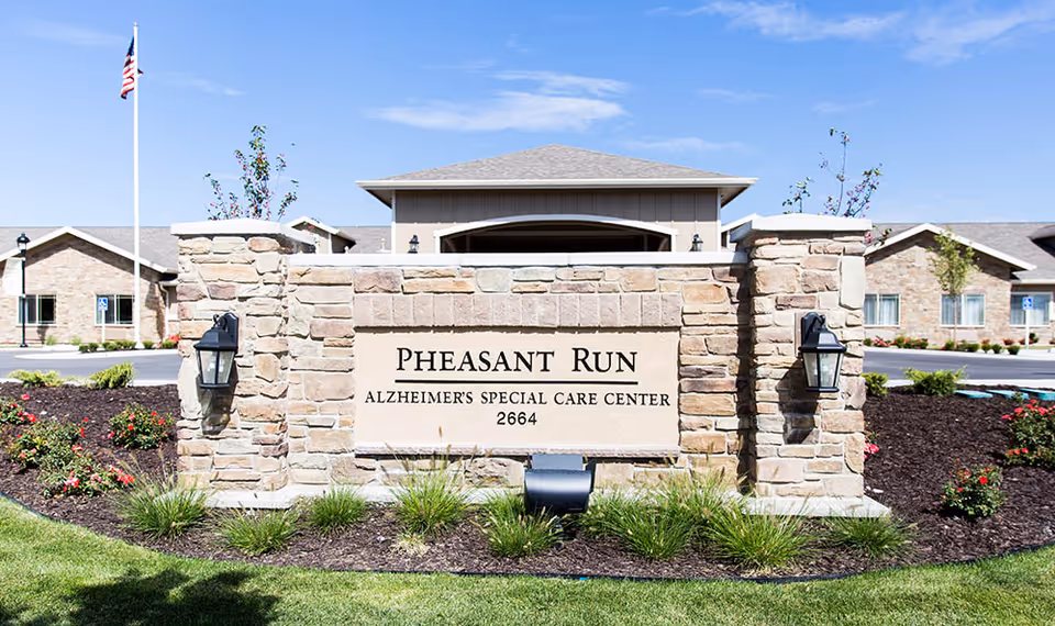 Stone entrance sign reading "PHEASANT RUN ALZHEIMER'S SPECIAL CARE CENTER 2664" in front of a single-story care building with lawn and landscaping.