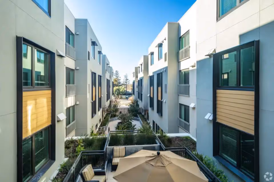 Landscaped central courtyard between modern multi-story residential buildings with outdoor seating and a patio umbrella.
