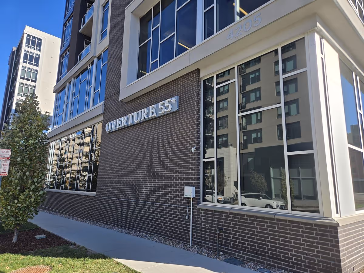 Exterior view of the Overture 55+ building's brick facade with large windows and signage.
