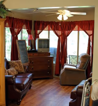 Cozy living room with red curtains, leather sofa, recliner chairs, TV, and ceiling fan.