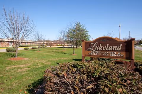 Front lawn and wooden sign for Lakeland Rehabilitation & Health Care Center with the building and clear blue sky in the background.