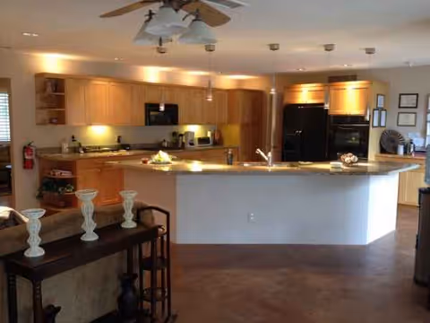 Open-concept kitchen with island, wooden cabinets, and appliances in a senior living facility.