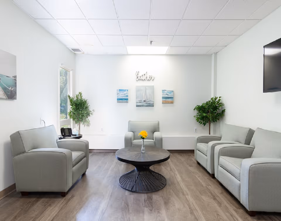 Bright lounge with grey sofas, round coffee table, and potted plants.