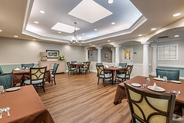 Spacious dining room with multiple set tables, wood flooring, decorative columns, and recessed ceiling lighting.