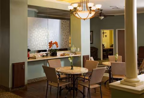 Cozy senior living dining area with round tables, chairs, and a serving counter.