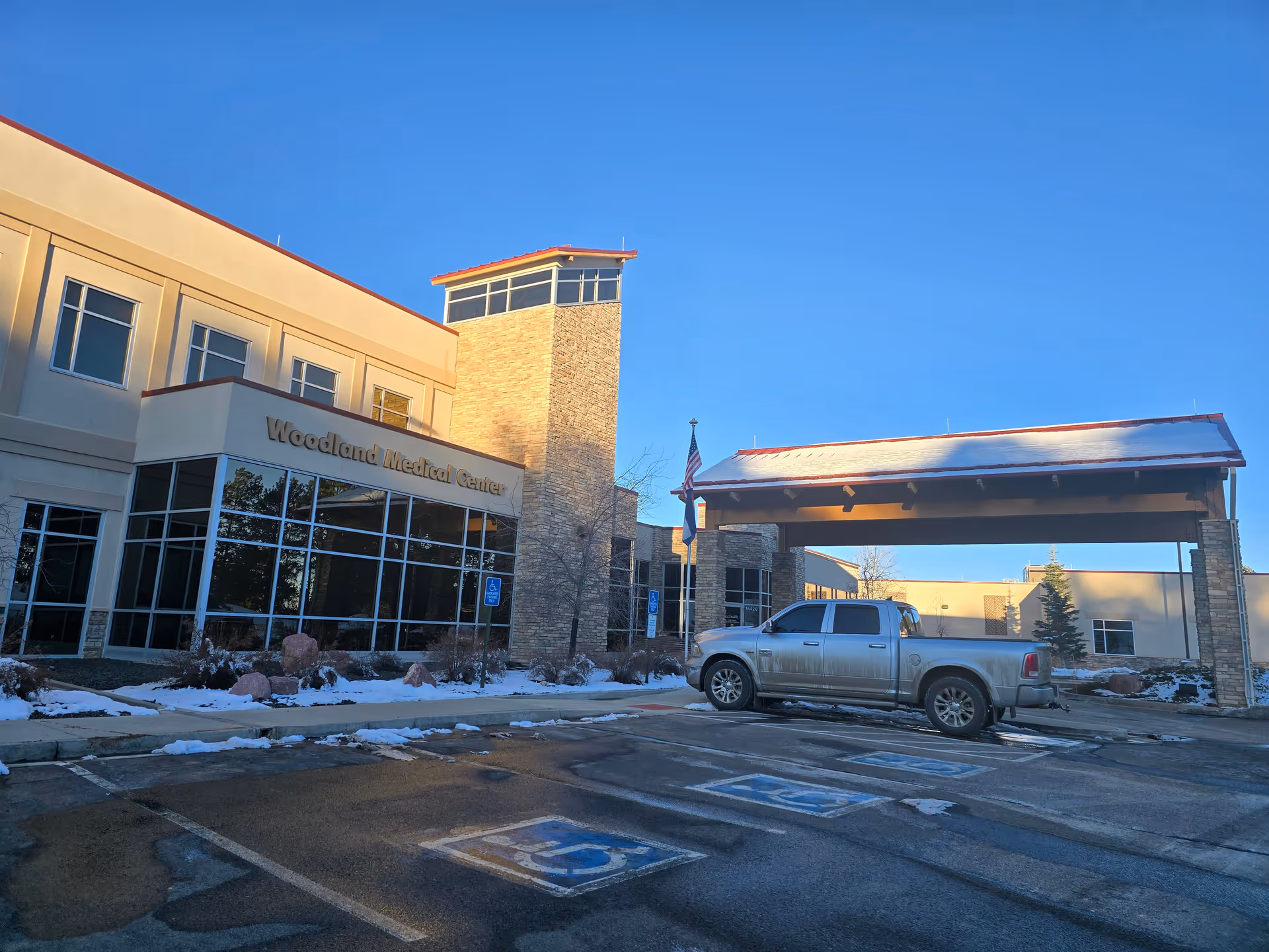 The front exterior of the Woodland Medical Center building with a covered drop-off, a parked pickup truck, and light snow on the ground.