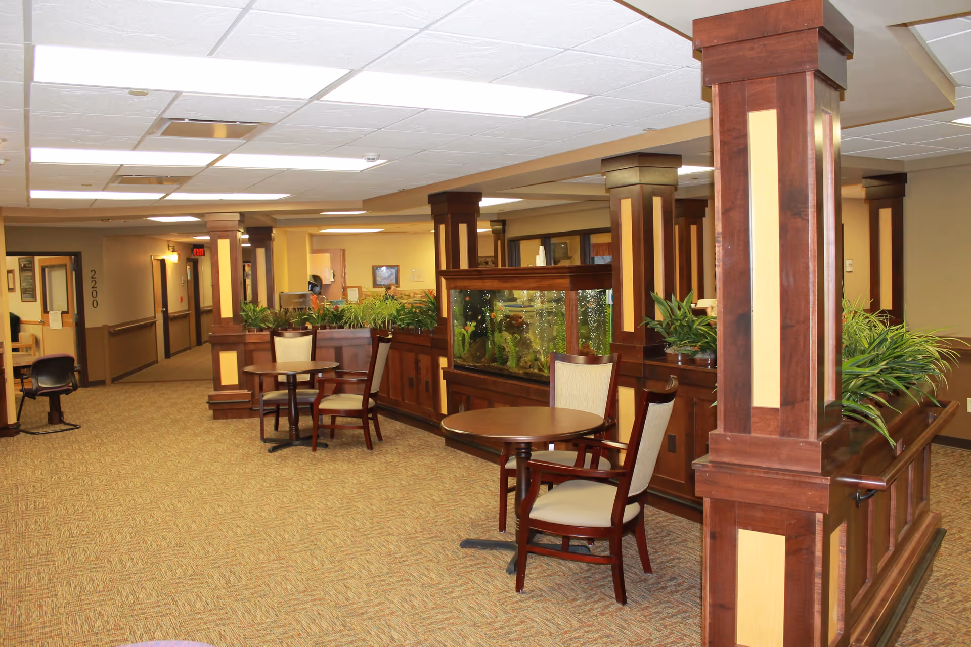 Common area with round tables and chairs, wooden columns, planter boxes and a large aquarium.