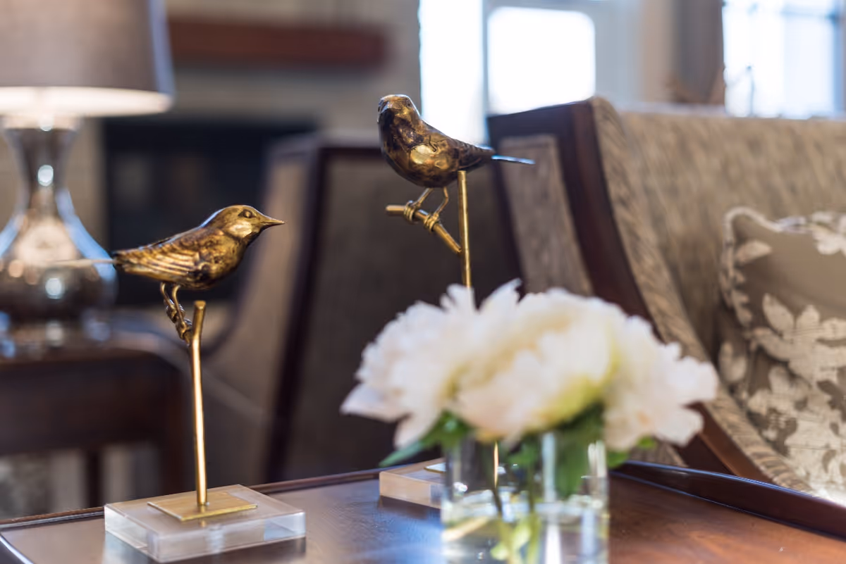 Decorative brass bird sculptures and a vase of white flowers on a wooden coffee table in a cozy living room seating area.