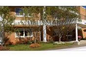 Exterior view of a brick building with white columns at the entrance, surrounded by small trees and landscaped greenery.