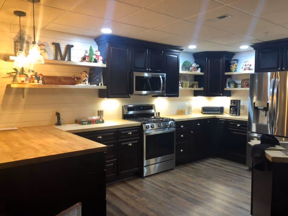 Well-lit kitchen with dark cabinets, stainless steel appliances, butcher-block counters and open shelves decorated for Christmas.