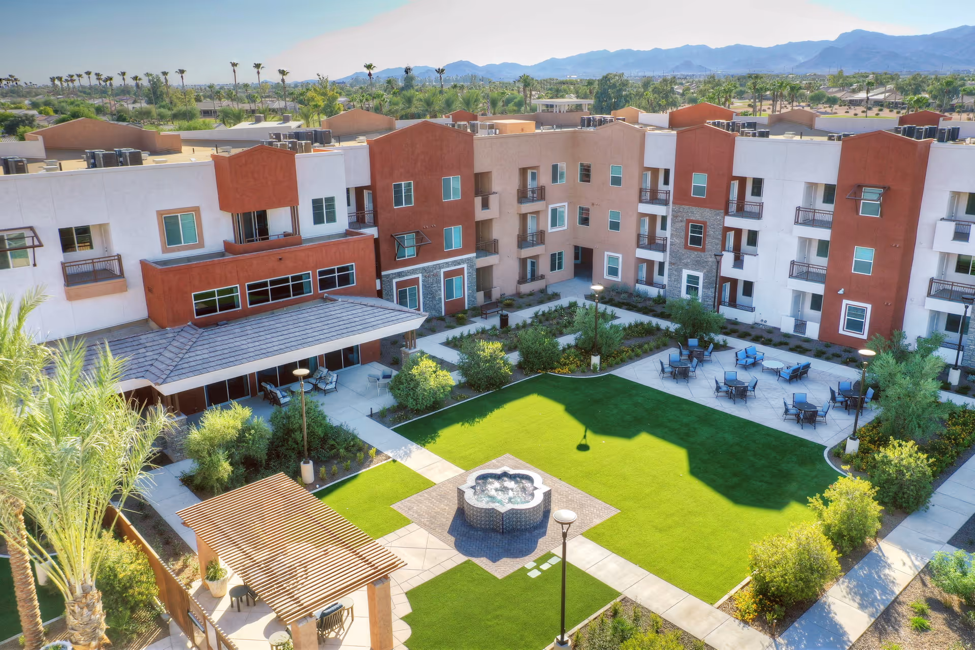 Aerial view of a senior living facility courtyard with a central lawn, fountain, seating areas, and surrounding multi-story buildings.