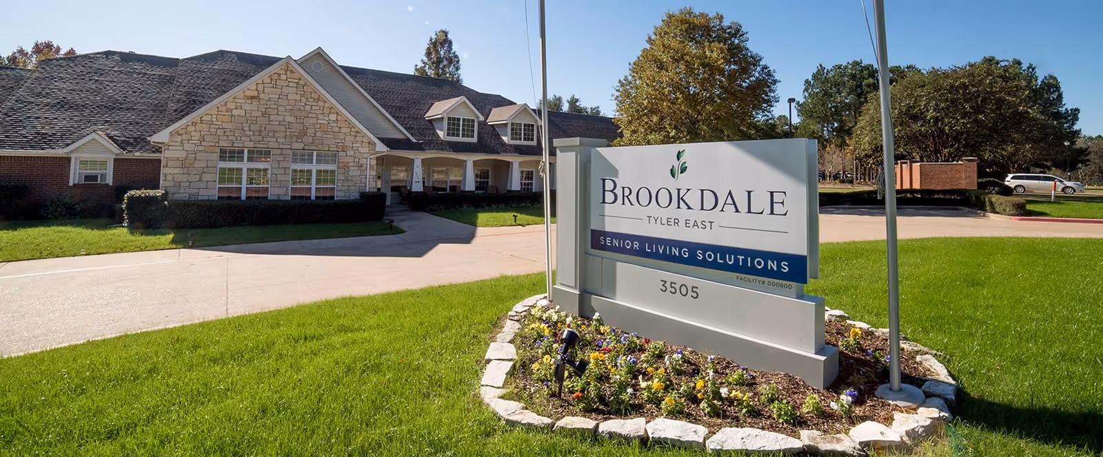 Exterior view of Brookdale Tyler East senior living facility with a stone and brick building, a driveway, green lawn, and a sign displaying the facility name and address 3505.