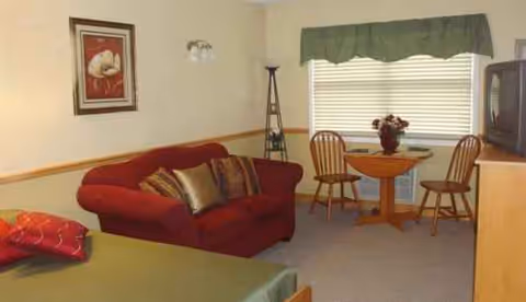 A cozy living room in a senior facility with red sofa, round table, and TV.