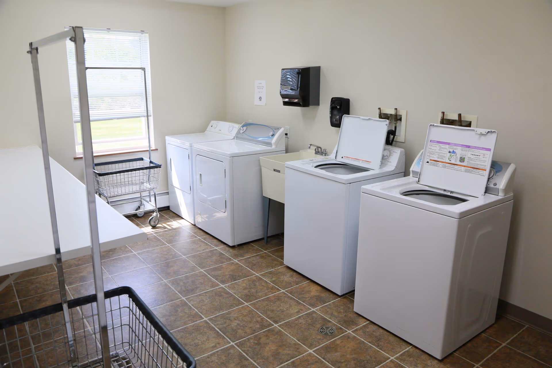 Laundry room with three top-loading washers, a dryer, utility sink, folding table, and laundry carts.