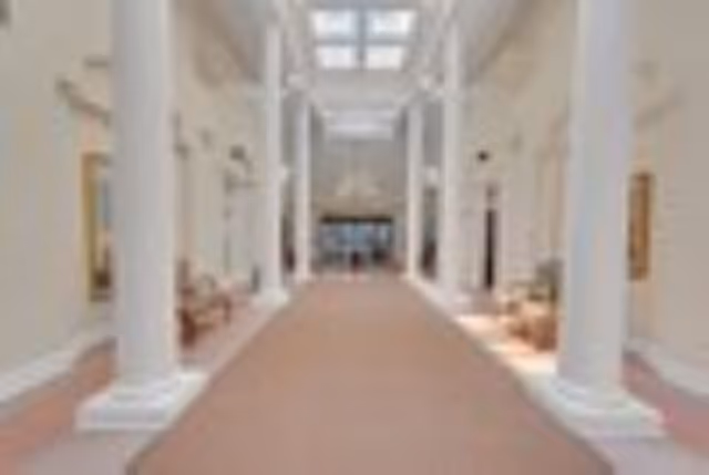 Bright wide interior corridor with tall white columns, skylights, and seating along the sides.