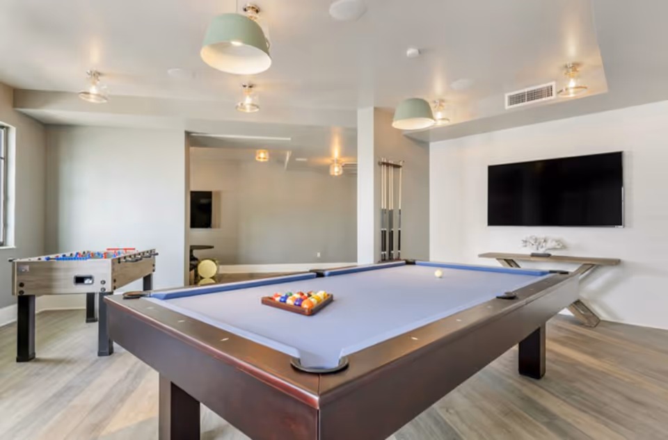 Bright recreation room with a pool table, foosball table, wall-mounted TV, and modern lighting.