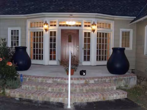 Front entrance of a residential building with brick steps, glass doors, and large planters.
