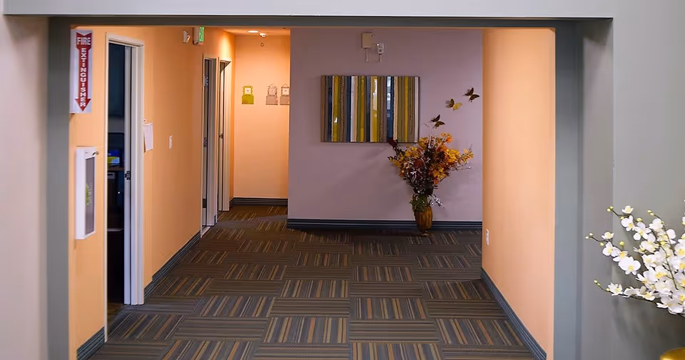 Hallway interior with striped carpet, peach-colored walls, wall art, and a vase of flowers at the end.