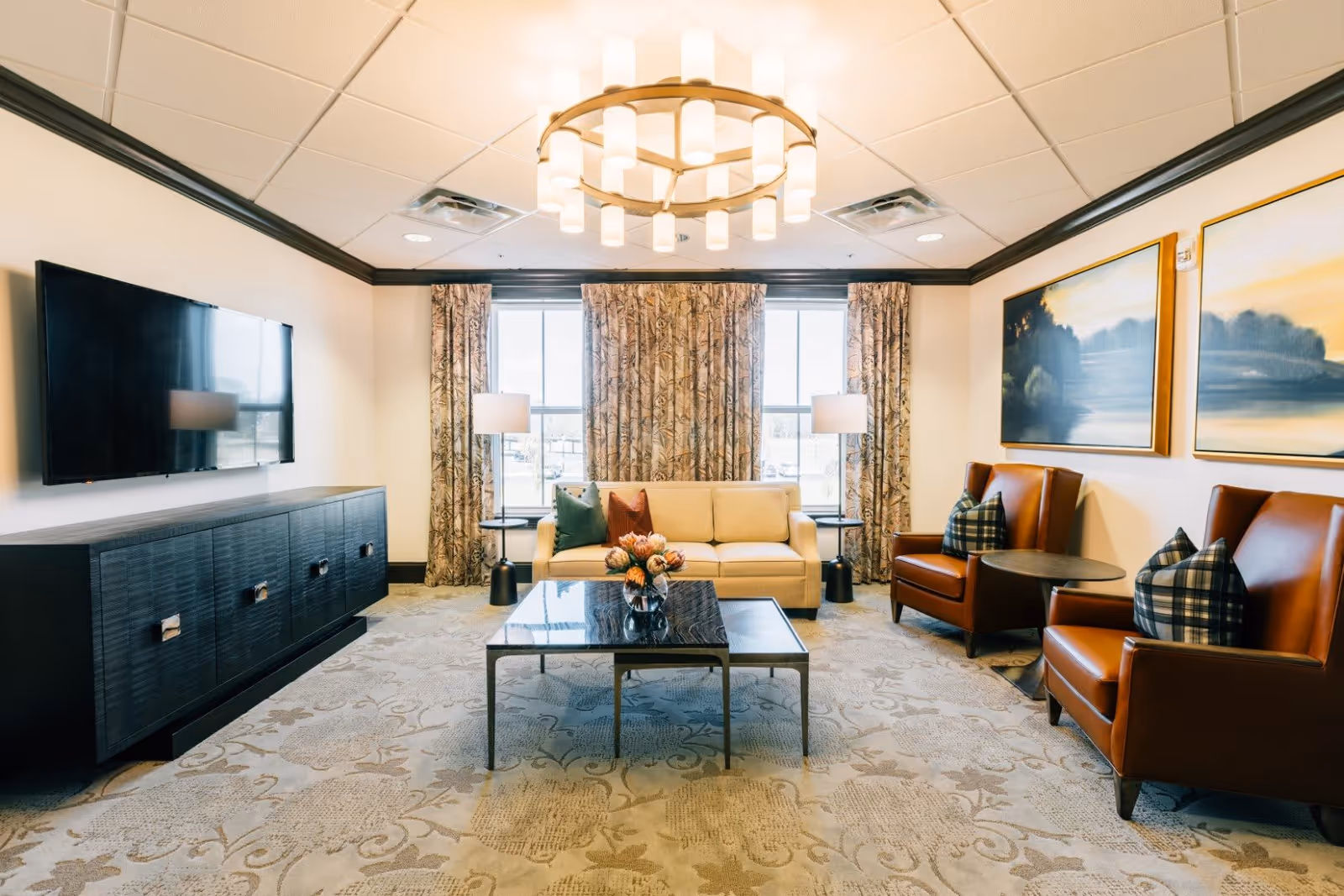 Bright, furnished common living room with a sofa, leather armchairs, coffee table, TV console and large windows.