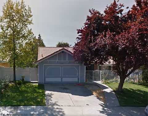 A single-story blue garage-front building with driveway, trees, and a small lawn.