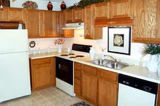 Kitchen area in a retirement community with wooden cabinets, white appliances, and sink.