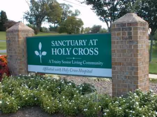 Green Sanctuary at Holy Cross sign between brick pillars with flower bed.